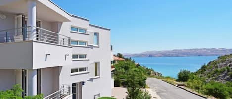 A modern two-story building with balconies, a paved driveway, and a view of a lake.