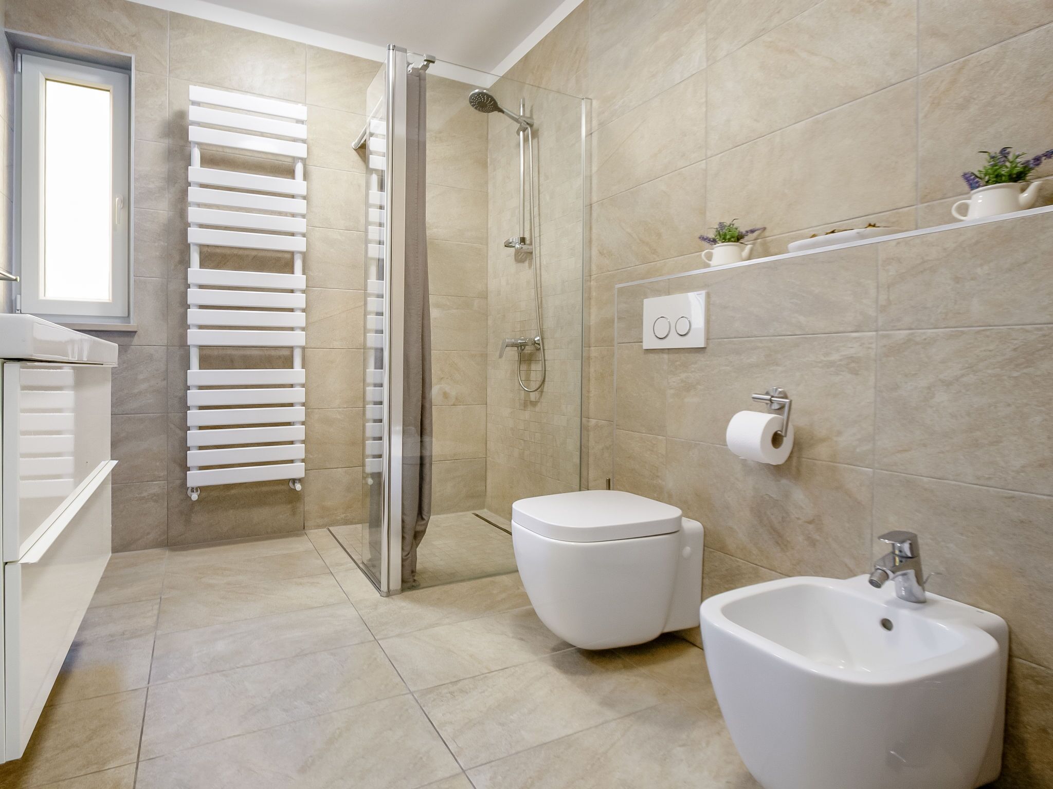 A modern bathroom with a glass-enclosed shower, a toilet, a bidet, and a sink.