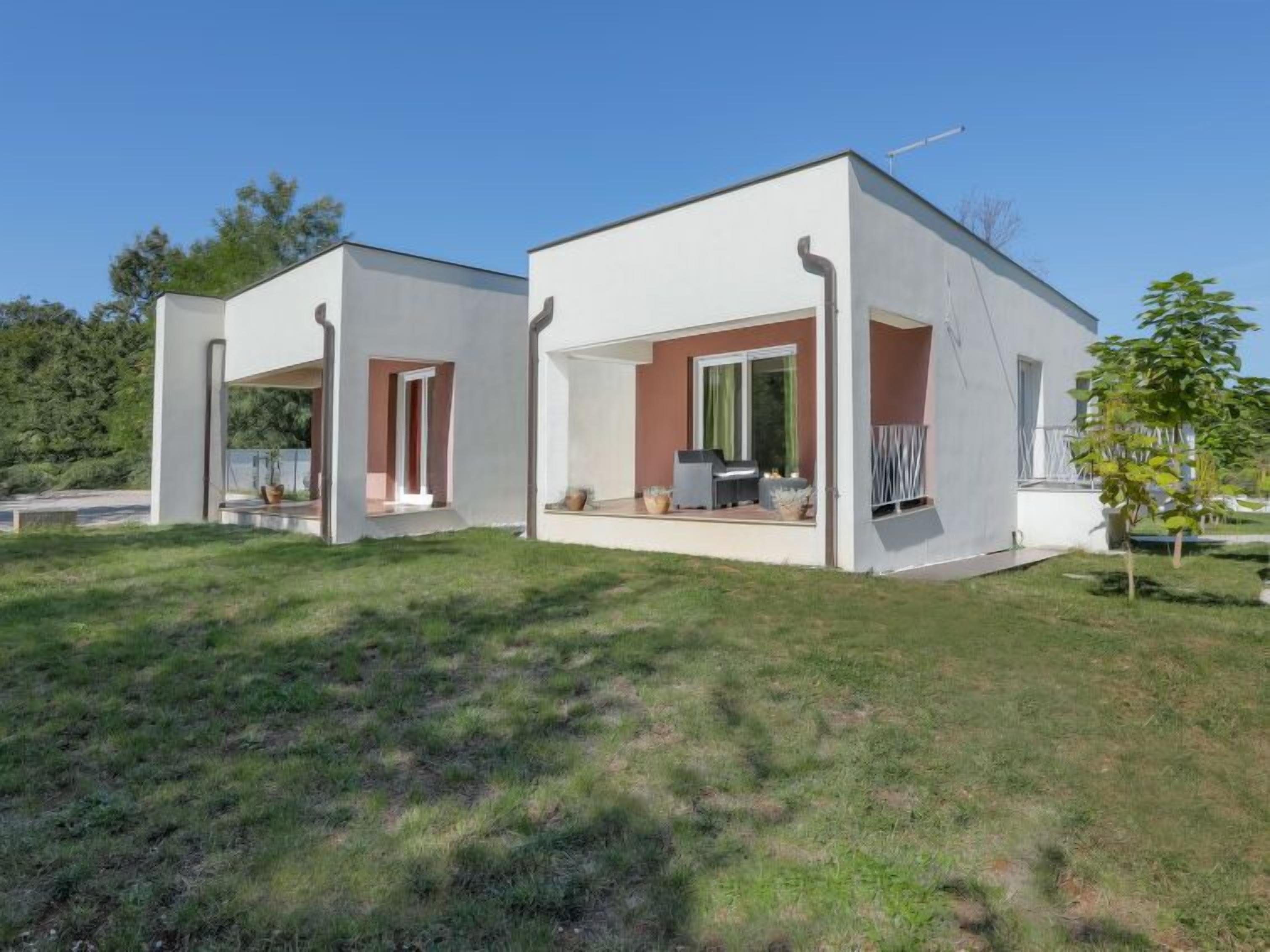 Una casa moderna de dos pisos con techo plano, ventanas amplias y un patio cubierto.