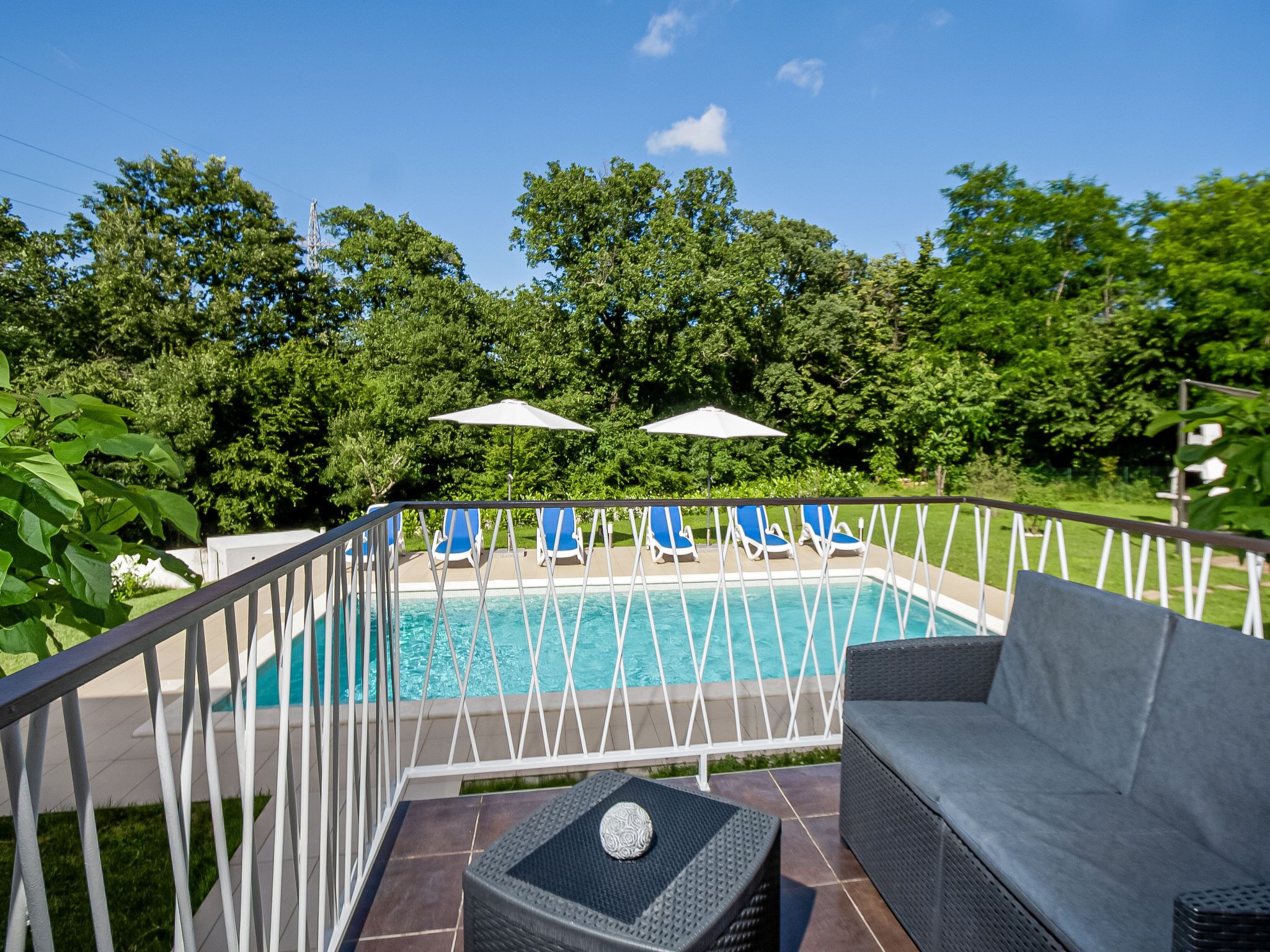 A poolside area with a pool, blue lounge chairs, a grey sofa, and a small table.