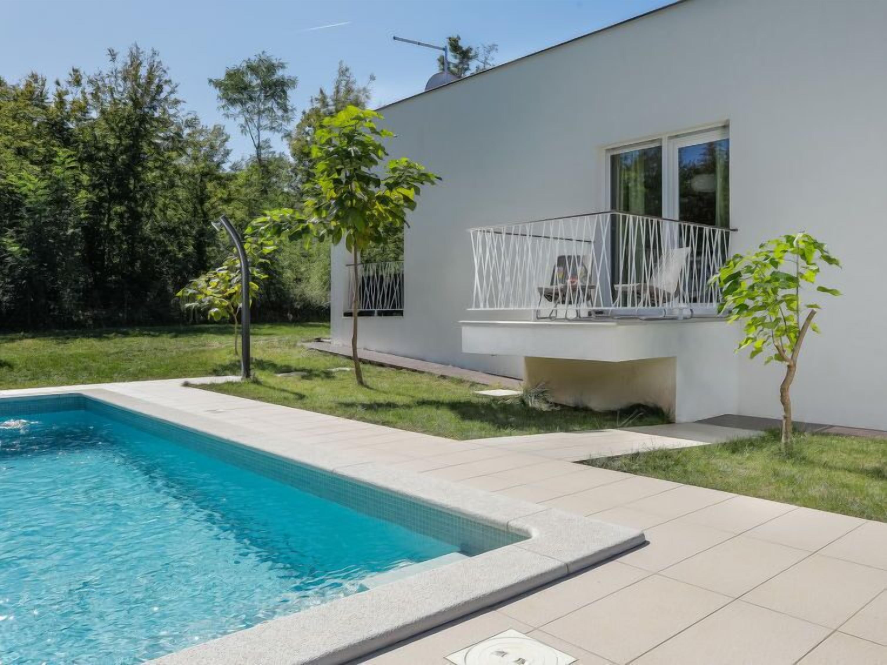 Una casa moderna con piscina, balcón y un pequeño jardín.