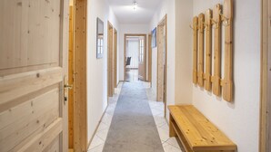 Un couloir avec des portes en bois, un banc et des crochets fixés au mur.