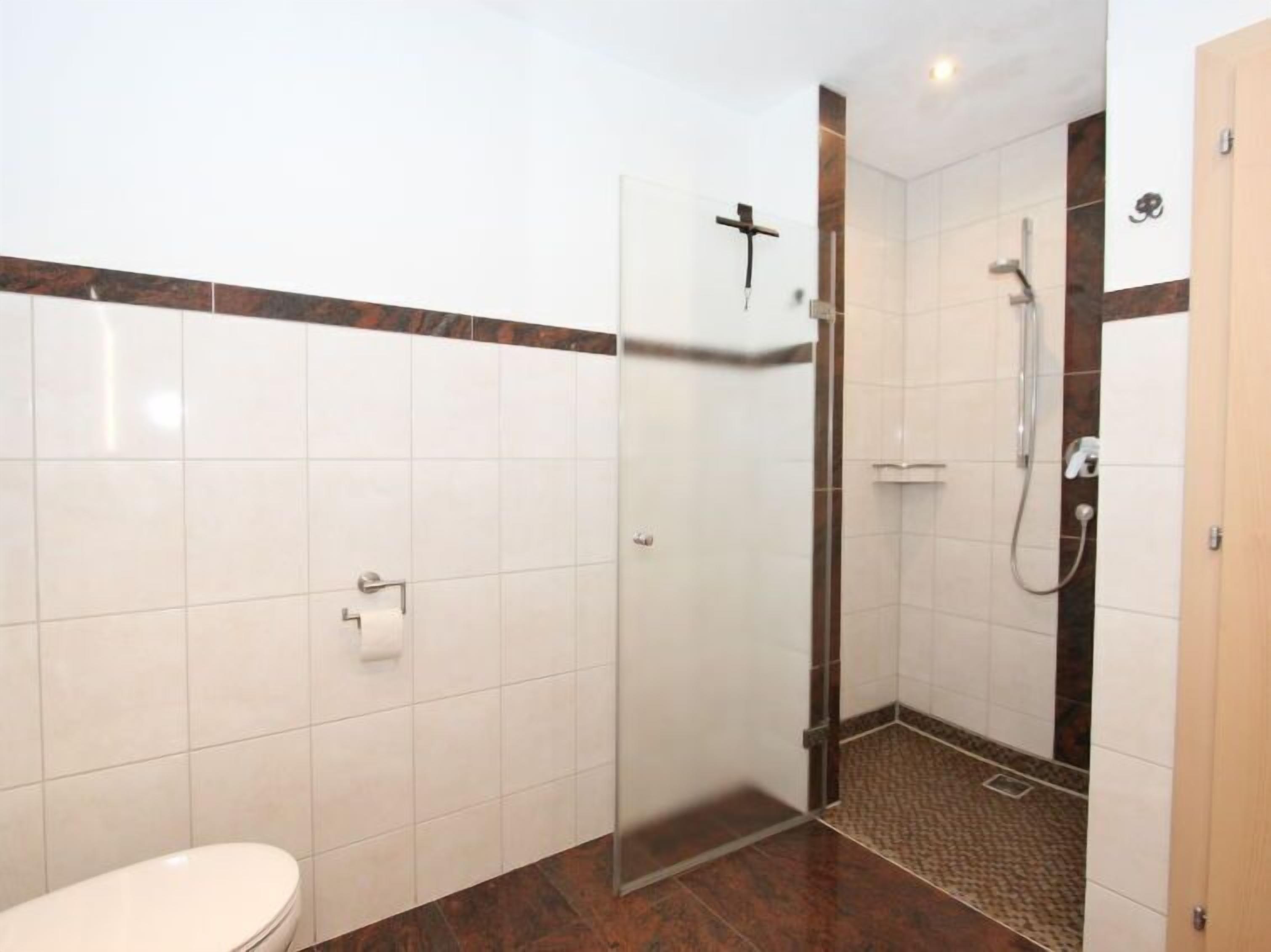 A modern bathroom with a shower, toilet, and a glass door shower stall.
