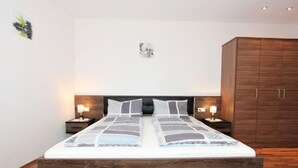 A bedroom with a wooden bed frame, two bedside tables with lamps, and a wardrobe. - Apartment Hanna by Interhome (Kaltenbach)