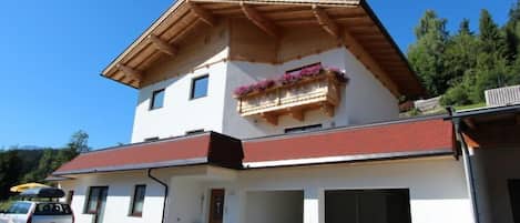 Ein zweistöckiges Gebäude mit rotem Dach, einem Balkon mit Blumenkästen und einem geparkten Auto davor.