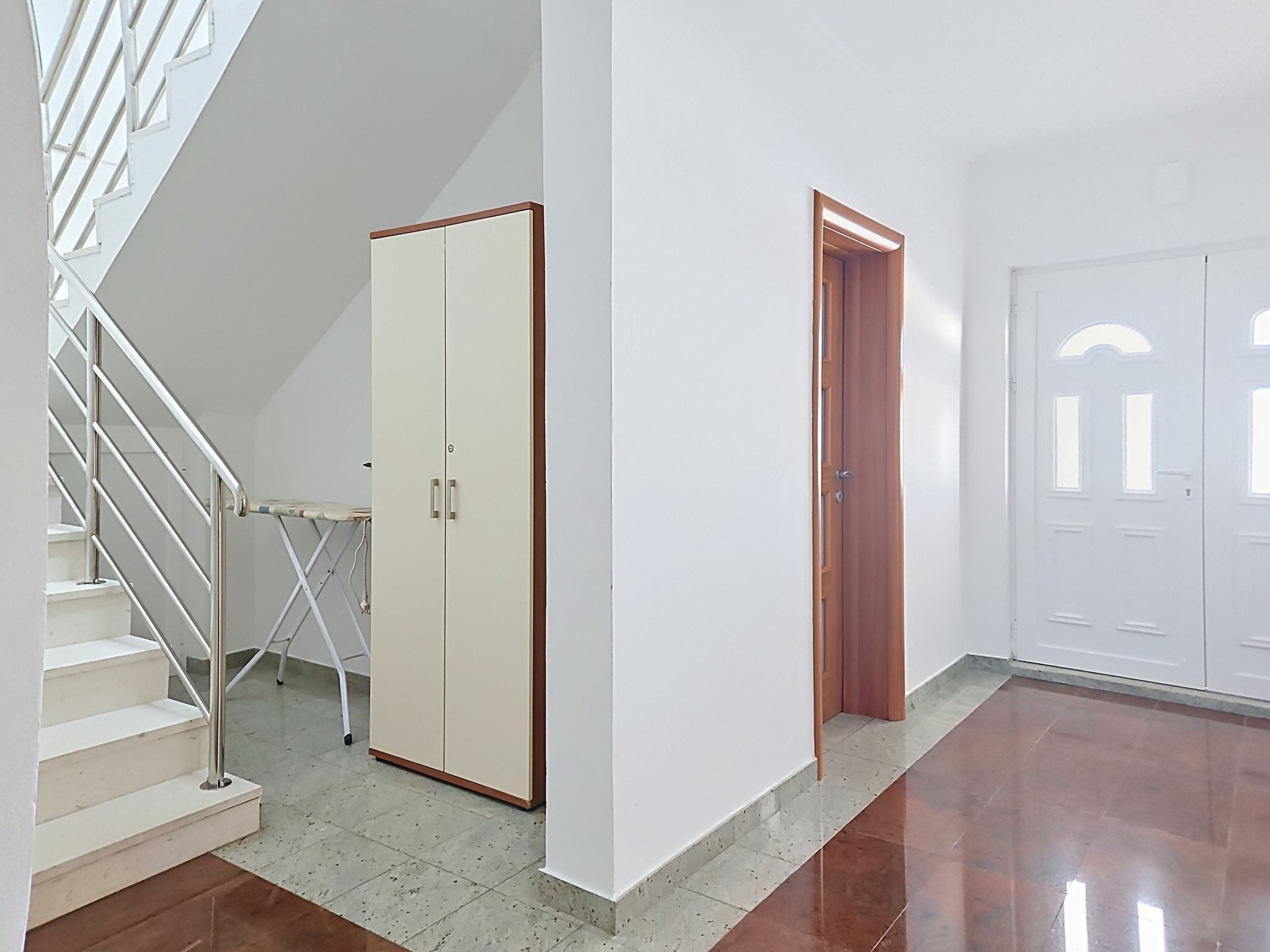 En trappe med metalgelændere, en beige garderobe, en trædør og en hvid dør med buede vinduer.