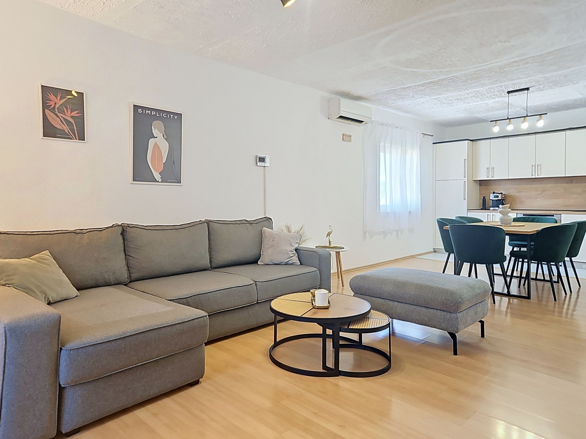 Ein modernes Wohnzimmer mit grauem Sofa, einem runden Couchtisch und einem Essbereich mit kleinem Tisch und Stühlen.