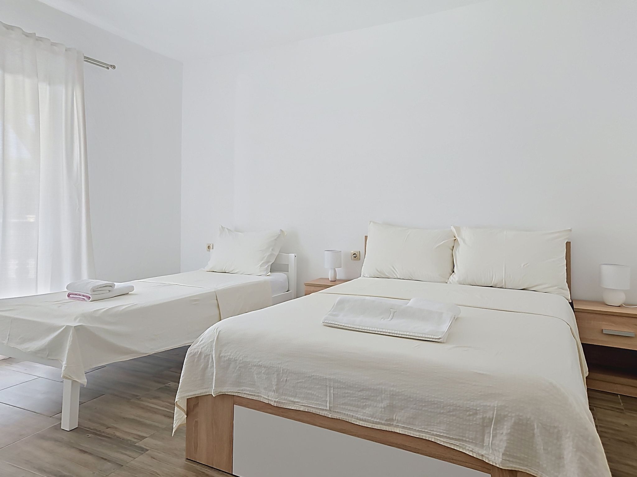 A hotel room with two single beds, a small table with a lamp, and a wooden floor.