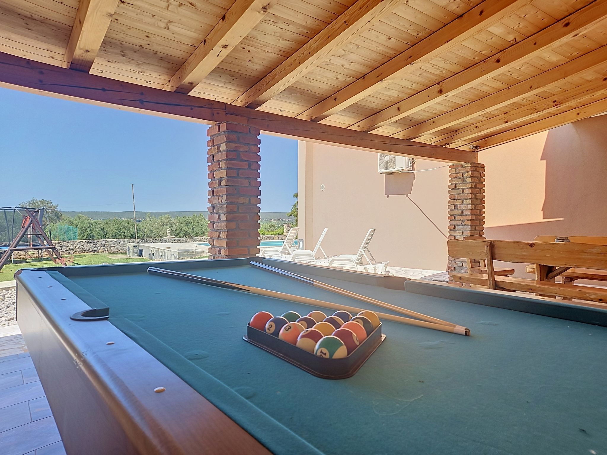 A pool table with a set of billiard balls, wooden beams, and a brick pillar.