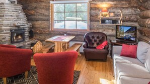 A cozy cabin interior with a stone fireplace, wooden furniture, and a television.