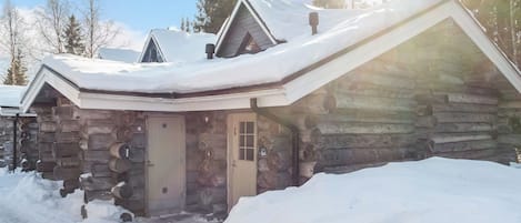 A log cabin with a snow-covered roof, a wooden door, and a chimney.