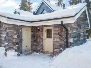 A log cabin with two doors, a chimney, and a snow-covered roof.