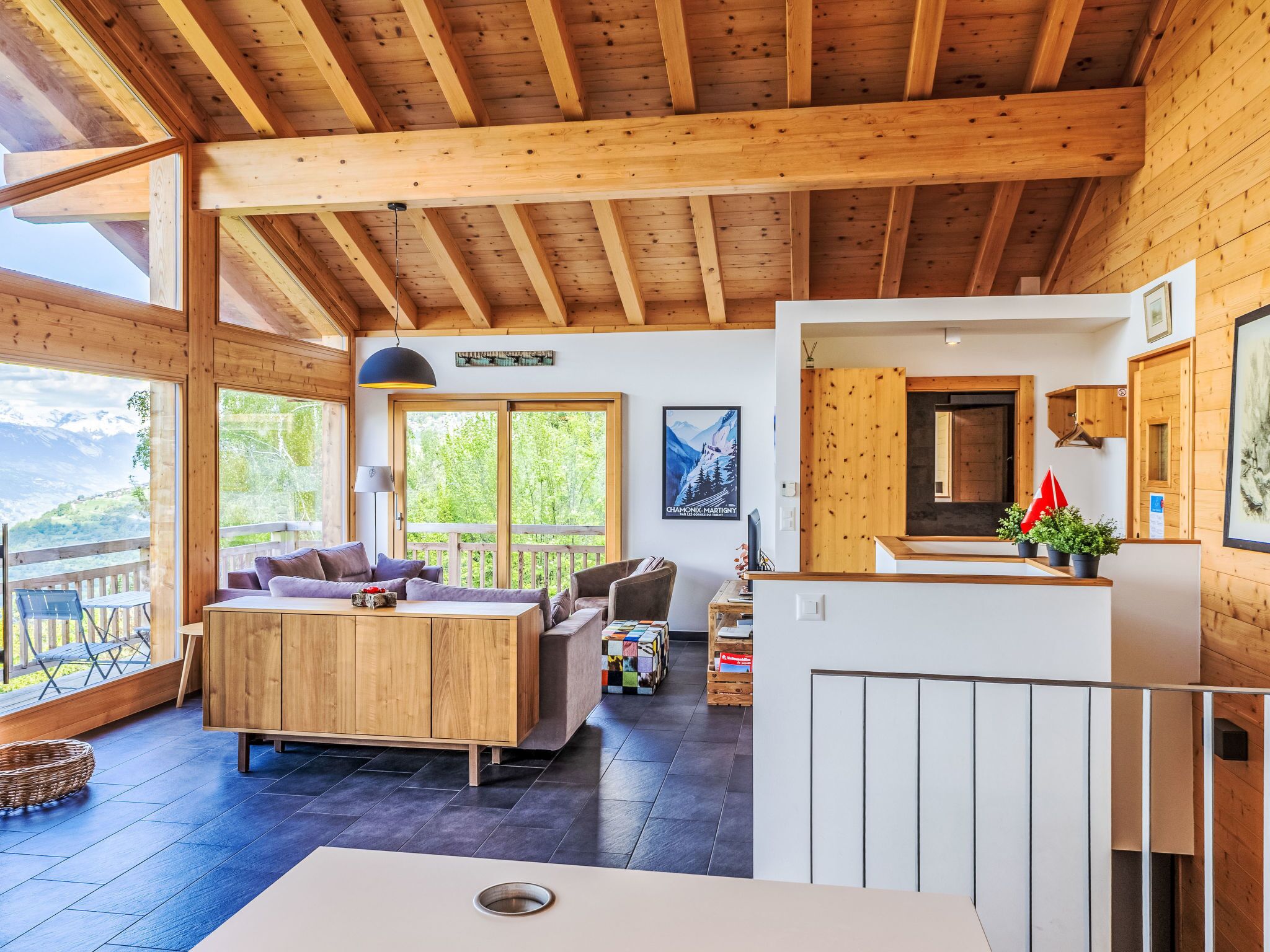 A wooden interior with a sofa, dining table, and a view of mountains through large windows.