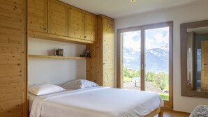 A wooden room with a bed, a shelf with items, and a view of mountains through a glass door. - Vacation home D'Arby by Interhome (Nendaz)