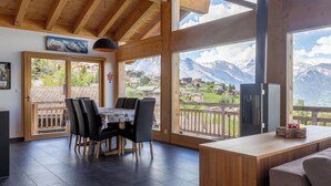 A spacious room with a wooden ceiling, a dining area with a table and chairs, and large windows offering mountain views. - Vacation home D'Arby by Interhome (Nendaz)