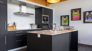A modern kitchen with a central island, stainless steel appliances, and wooden ceiling beams. - Vacation home D'Arby by Interhome (Nendaz)