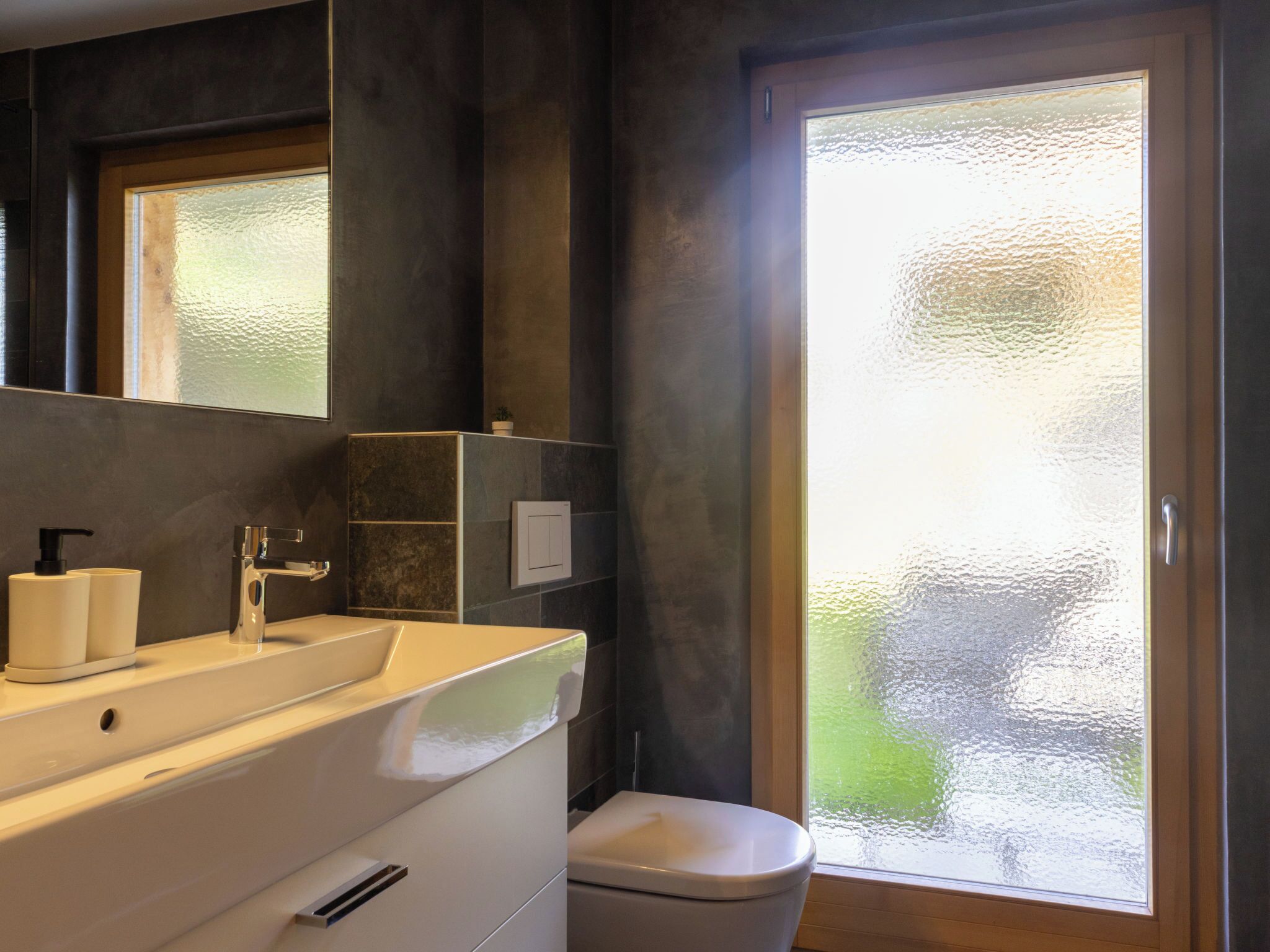 Une salle de bain moderne avec un grand miroir, un lavabo blanc, des toilettes et une porte en verre dépoli.