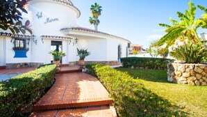 A white building with a curved facade, a tiled entrance, and a well-maintained garden with palm trees and shrubs. - Zurbarán by the Sea by Interhome (Rincón de la Victoria)