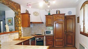 A kitchen with wooden cabinets, a stone arch, a microwave, and a tiled floor. - La Péguière by Interhome (La Cadière d'Azur)