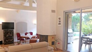 A spacious living area with a sofa, a dining table with chairs, a fireplace, and a TV mounted on the wall. - La Péguière by Interhome (La Cadière d'Azur)