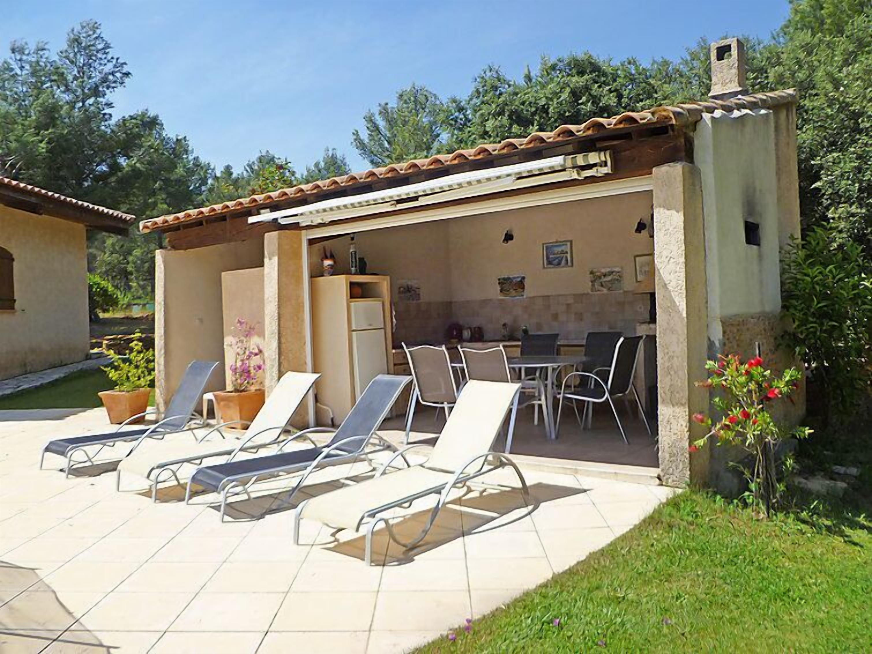 A covered outdoor patio with lounge chairs, a table, and a kitchen area.
