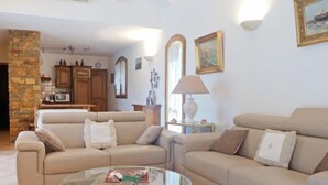 A living room with two beige sofas, a glass coffee table, and a kitchen area in the background. - La Péguière by Interhome (La Cadière d'Azur)