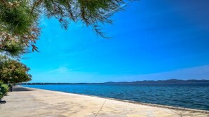 A paved waterfront promenade with a clear view of the sea and distant mountains.