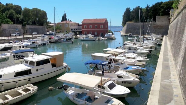 A marina with various boats docked, a red building, and a stone wall.