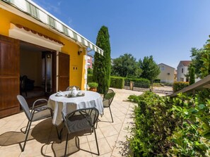 Une terrasse avec une table ronde et des chaises, un bâtiment jaune et un ciel bleu clair.