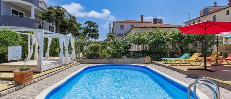 A swimming pool with a stone deck, surrounded by lounge chairs and a white gazebo.