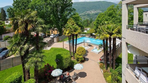 Un hotel con piscina, mobiliario exterior y abundante vegetación.