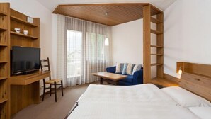 Una habitación de hotel con una cama, un escritorio con televisor, un sofá y una estantería de madera.