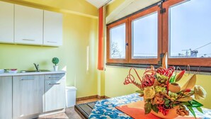 A room with a bed, a window with curtains, a small table with a vase of flowers, and a kitchen area with cabinets and a sink. - Apartment Ulika by Interhome (Poreč/Tar)