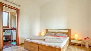 A bedroom with a wooden bed, two bedside tables with lamps, and a view of a bathroom through an open door. - Apartment Ulika by Interhome (Poreč/Tar)