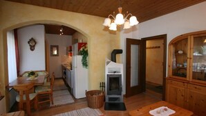 Een gezellige woonkamer met een houten plafond, een open haard, een eethoek met een tafel en stoelen, en een keuken die zichtbaar is door een boog.