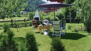 Een terras met stoelen en een tafel, omgeven door groen en een houten hek.