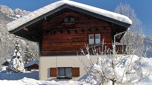 Een houten chalet met een schuin dak, grote ramen en een balkon.
