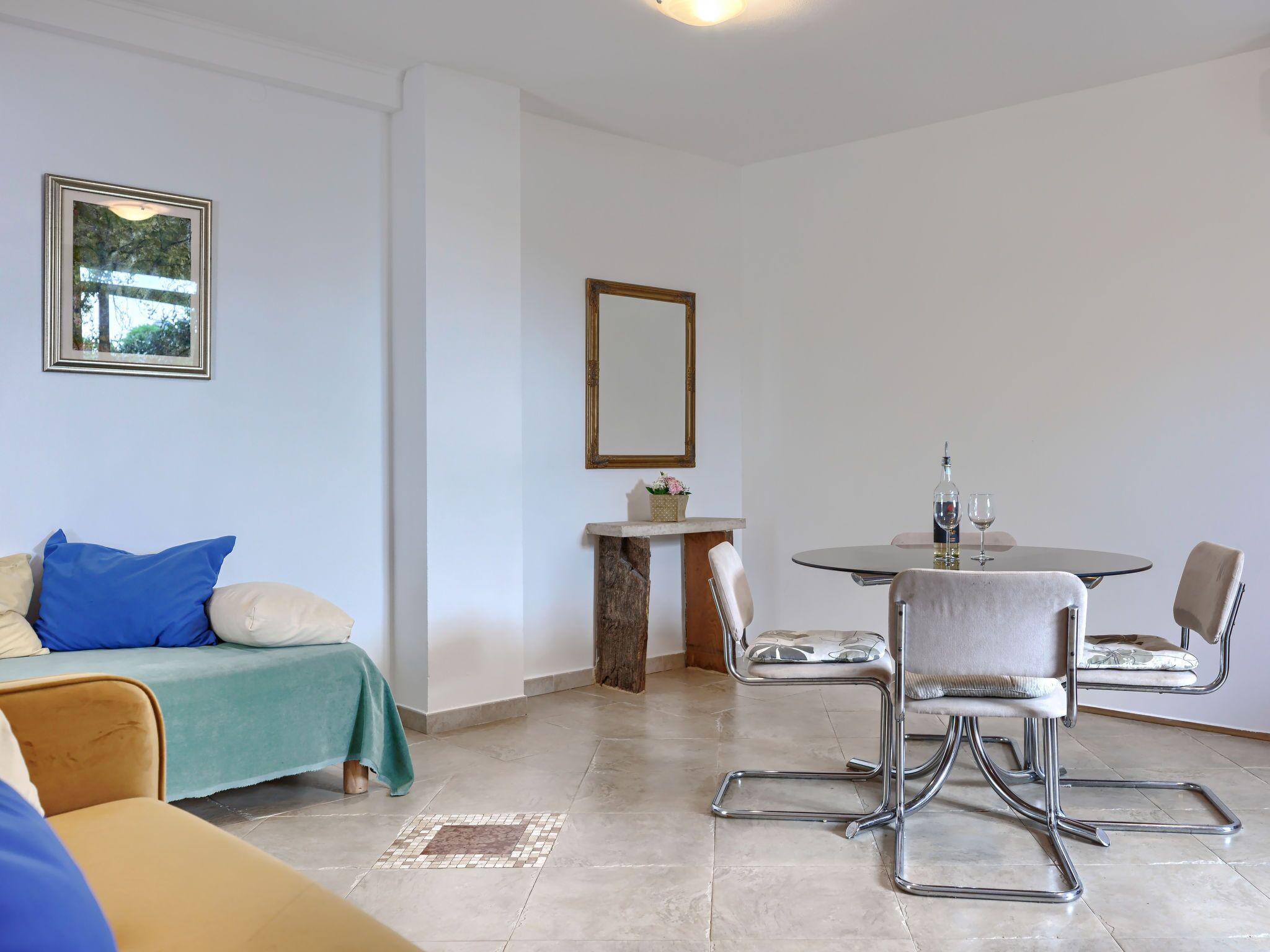 A room with a sofa, a dining table with chairs, a small side table, and a mirror on the wall.