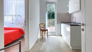 Een compacte hotelkamer met een bed, een stoel, een kitchenette en een deur naar een balkon.