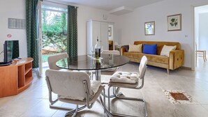 Een moderne woonkamer met een glazen eettafel, twee comfortabele stoelen, een bank met een blauw kussen, een kast en een televisie.