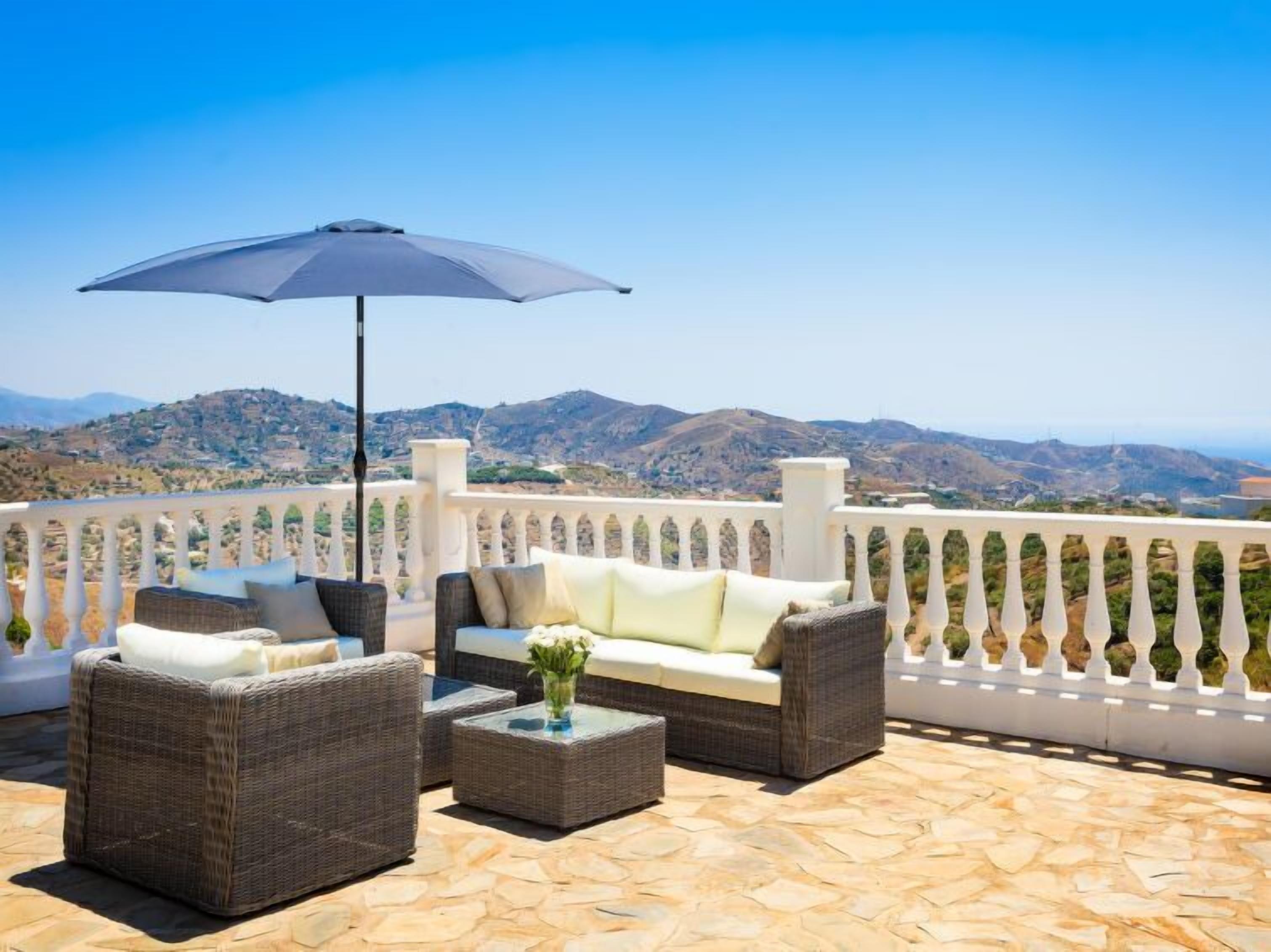 Une terrasse aménagée avec des meubles en osier, une table et un parasol. La terrasse offre une vue sur un paysage montagneux.