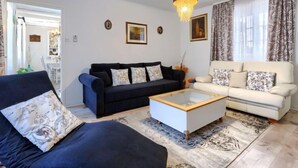 A living room with a dark blue sofa, a white sofa, and a glass coffee table. There is a chandelier hanging from the ceiling.