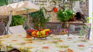 A table with a floral tablecloth, a fruit bowl, and outdoor seating with umbrellas.