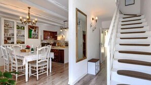 A spacious dining area with white chairs and a wooden table, a kitchen with wooden cabinets, and a staircase with wooden steps.