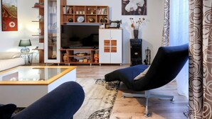 A modern living room with a sofa, a coffee table, a TV, a bookshelf, and a decorative chandelier.