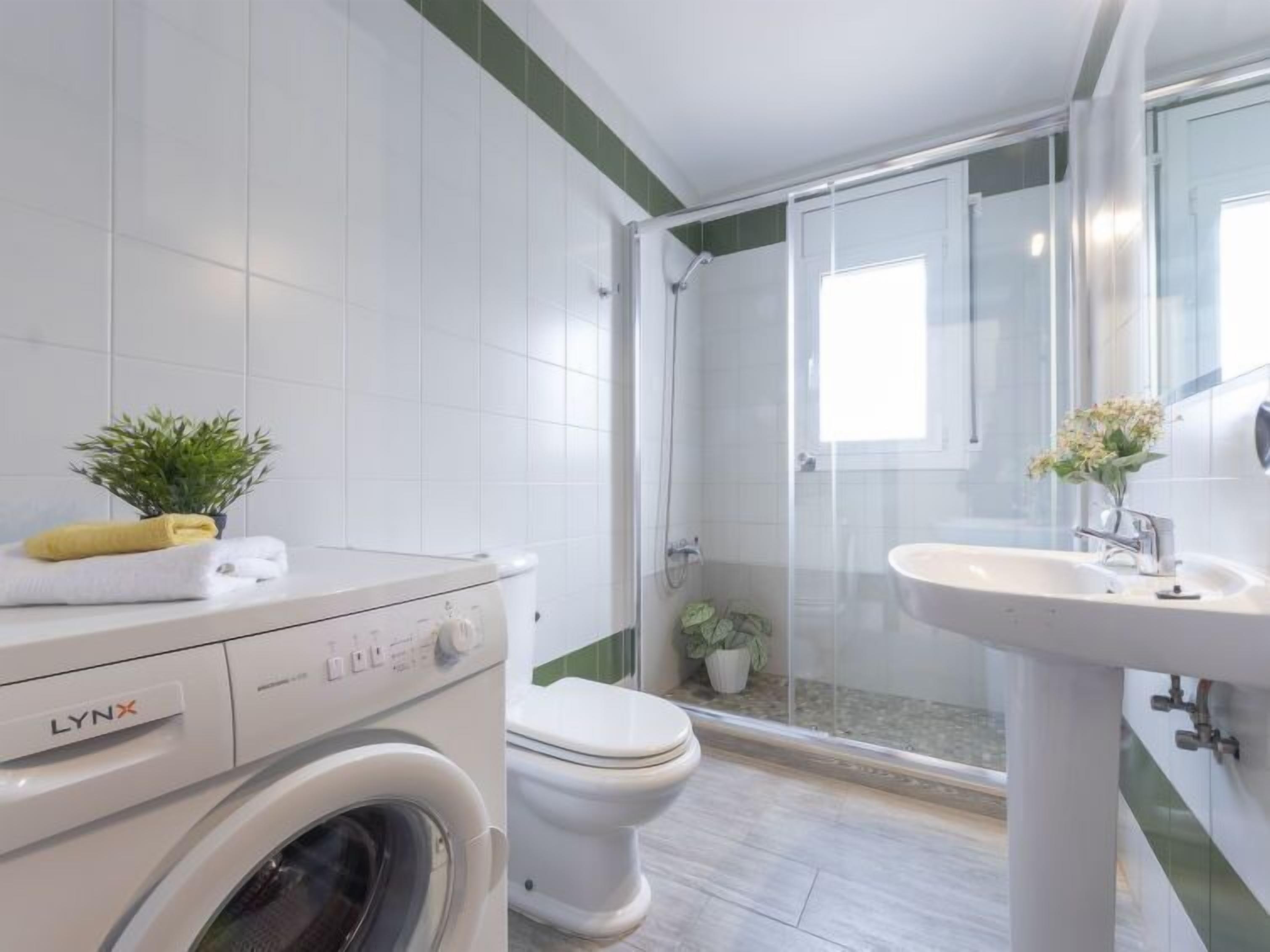 A modern bathroom with a washing machine, toilet, and glass-enclosed shower.