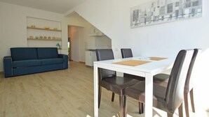 A modern living room with a blue sofa, a dining table with chairs, and a kitchen in the background. - Apartment Mira by Interhome (Umag)