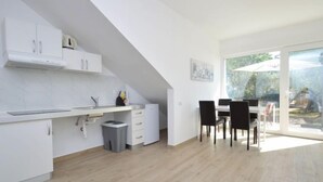 A modern kitchen with white cabinetry, a dining area with black chairs, and a large sliding glass door leading to an outdoor space. - Apartment Mira by Interhome (Umag)