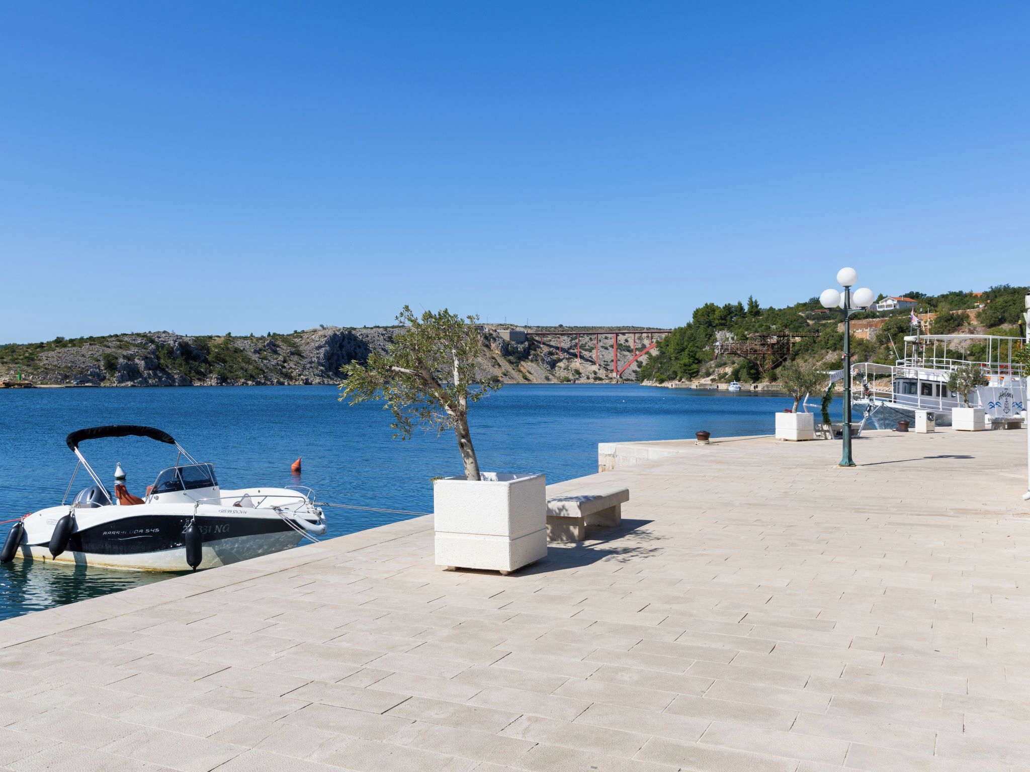 A marina with a boat docked, a clear sky, and a rocky coastline in the background.