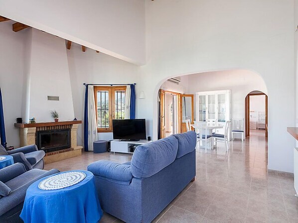 A spacious living room with a fireplace, a television, a sofa, and a dining area with a table and chairs.